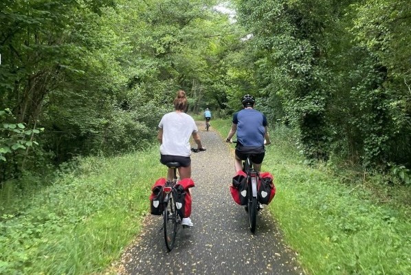 Couple à vélo avec sacoches rouges sur un chemin forestier ombragé, randonnée cycliste en pleine nature.